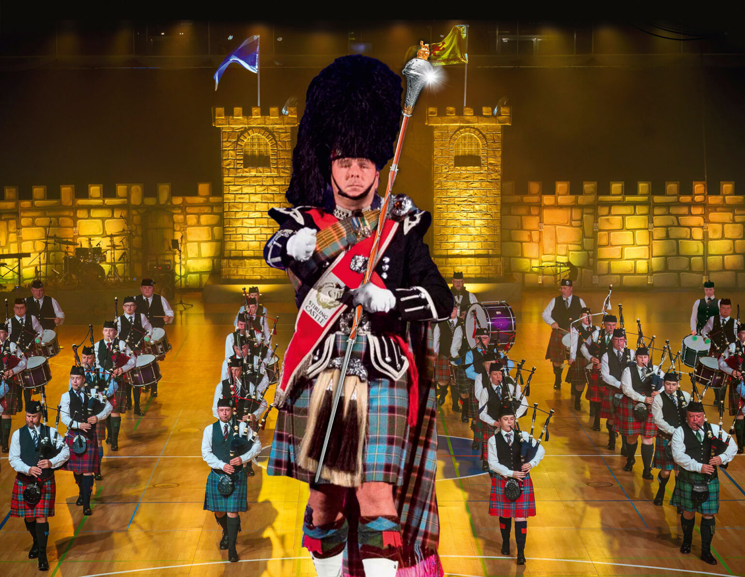 Schottische Pipe Band mit Tambourmajor, Dudelsackspielern und Trommlern bei einem Konzert vor einer beleuchteten Burgkulisse.